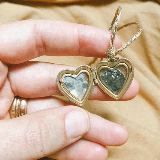 A hand holding a locket with two black and white portraits inside
