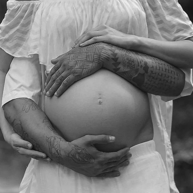 A black and white photo of a pregnant belly and two sets of arms wrapped around it.
