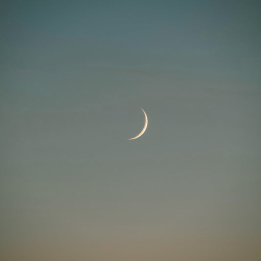 A small sliver of the moon in a dusky blue sky.